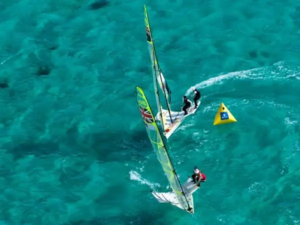Two 49er skiffs round a yellow race mark on turquoise water, seen from above